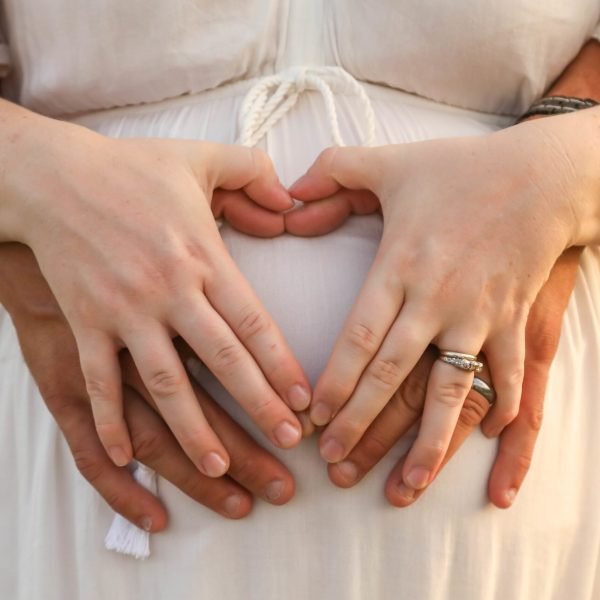 The married couple forming a heart shape with hands on the pregnant belly of the woman