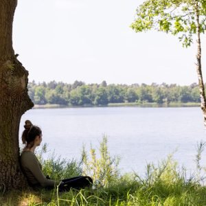 Young brunette woman sitting in green forest enjoys the silence and beauty of nature watching over a blue forest lake on a summer day. High quality photo