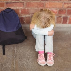 Sad pupil sitting alone on ground at corridor